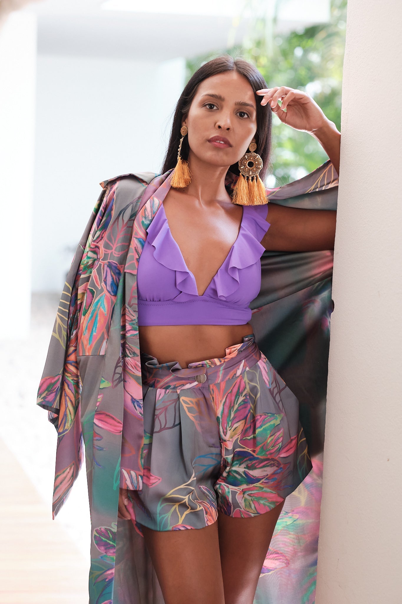 Woman kneeling against the wall wearing an all over tropical kimono duster made from recycled materials