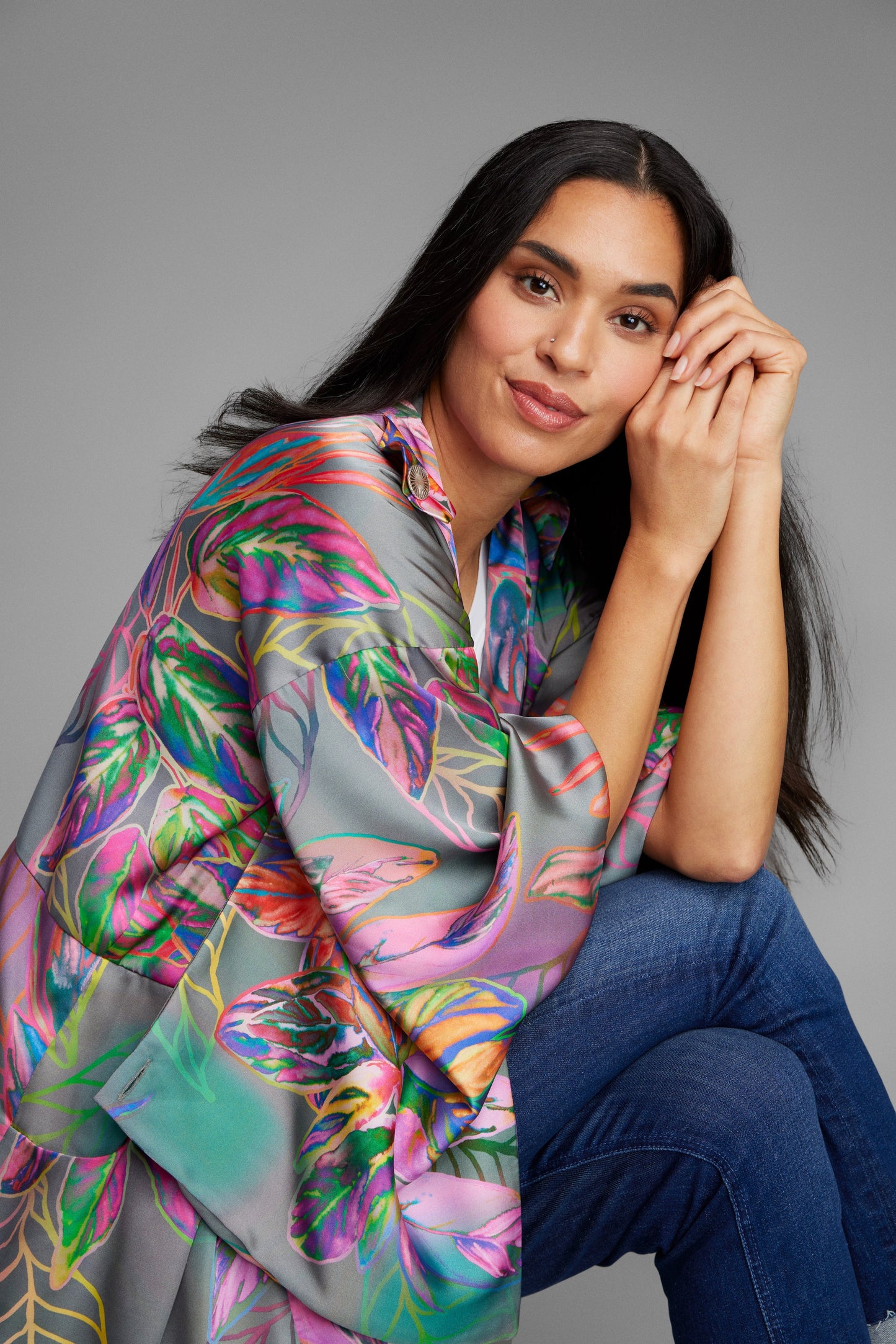 Woman sitting crossed legged wearing an all over tropical print kimono duster made from recycled materials