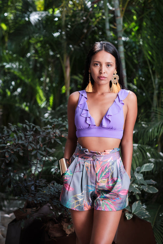 Woman sitting in nature modelling a purple top and tropical print tulip shorts made from recycled materials