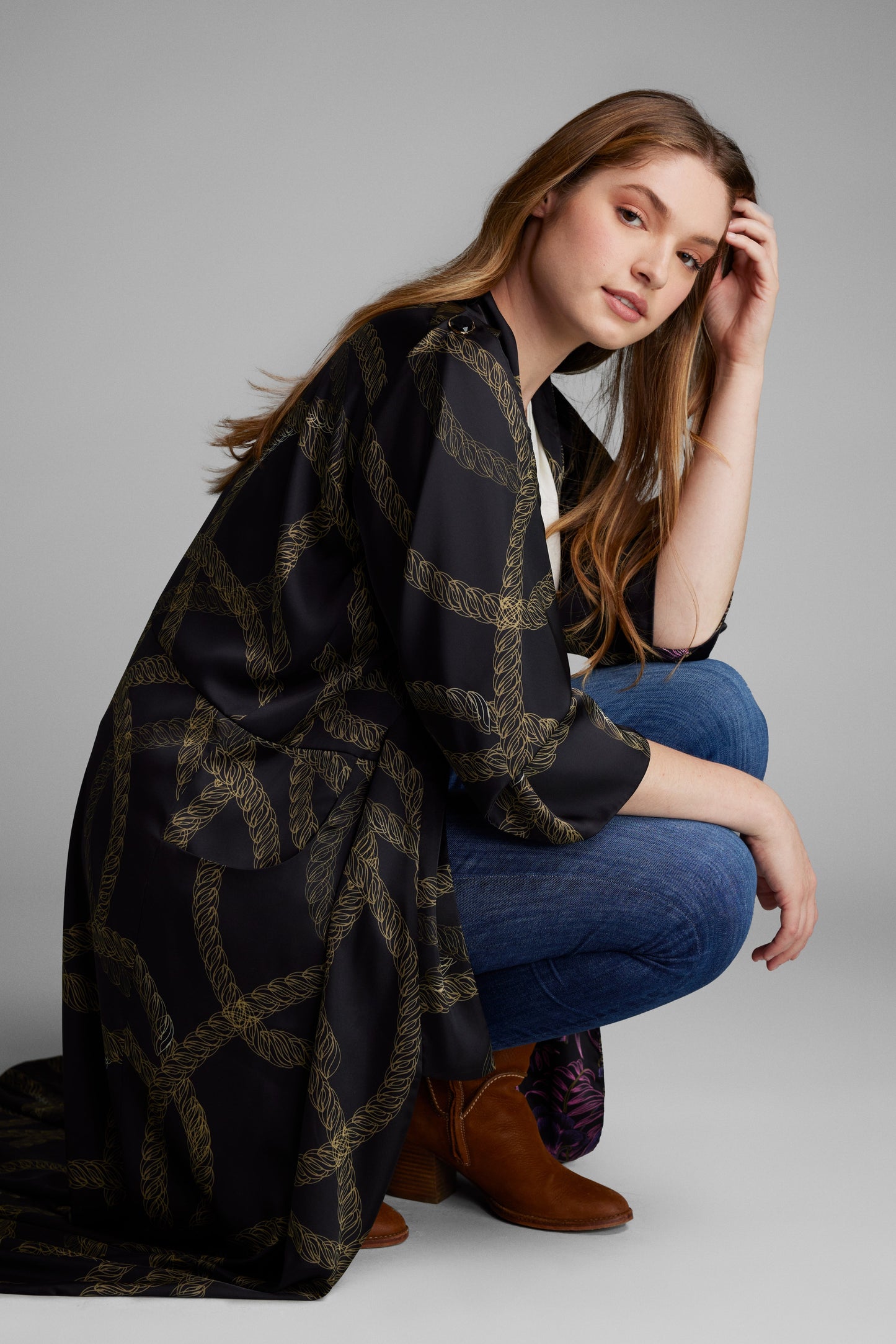 Woman kneeling down with a black and gold chain printed kimono duster made from recycled materials