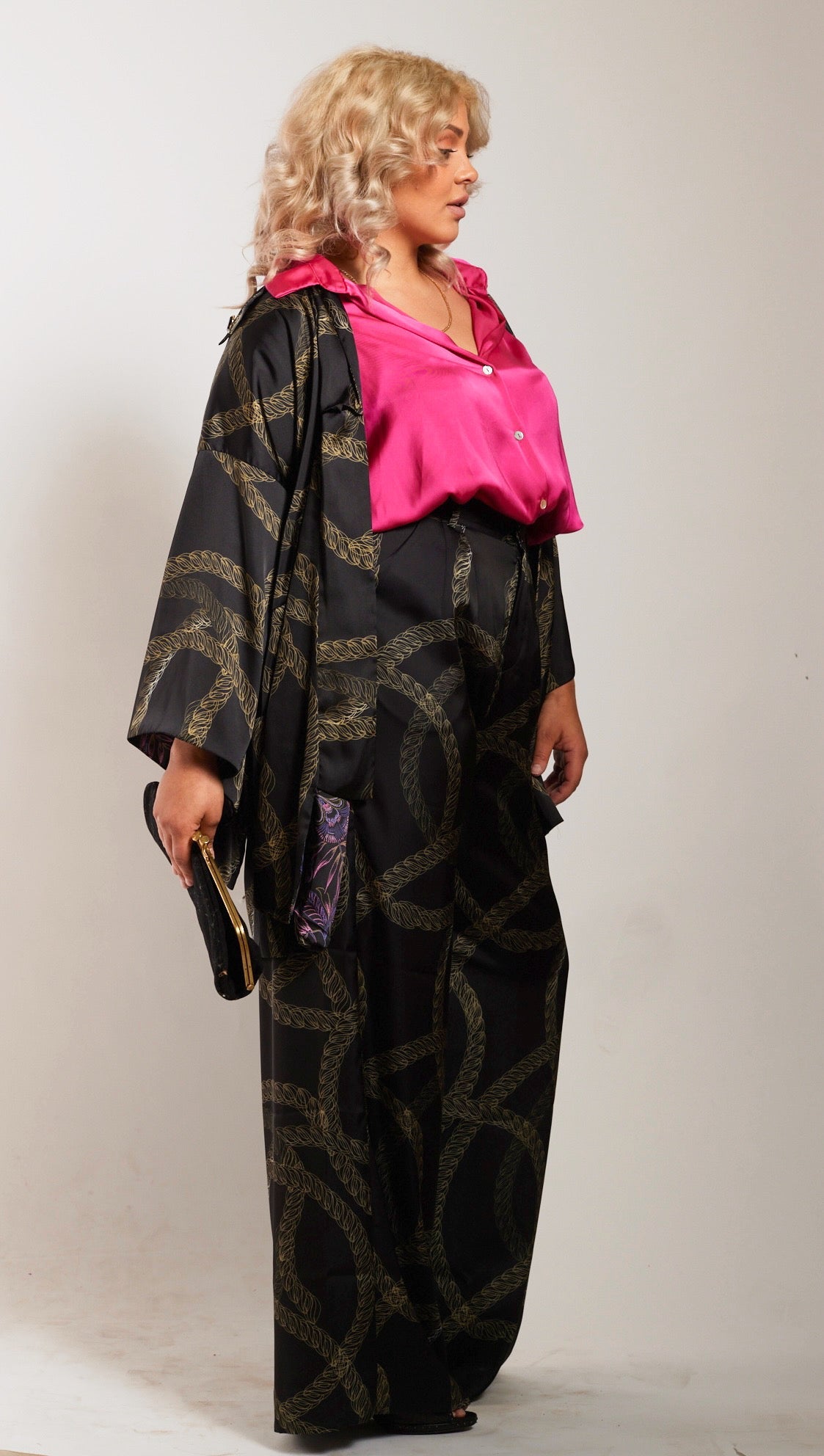 side profile woman modelling black and gold chains printed kimono duster with matching yacht slacks holding a clutch purse