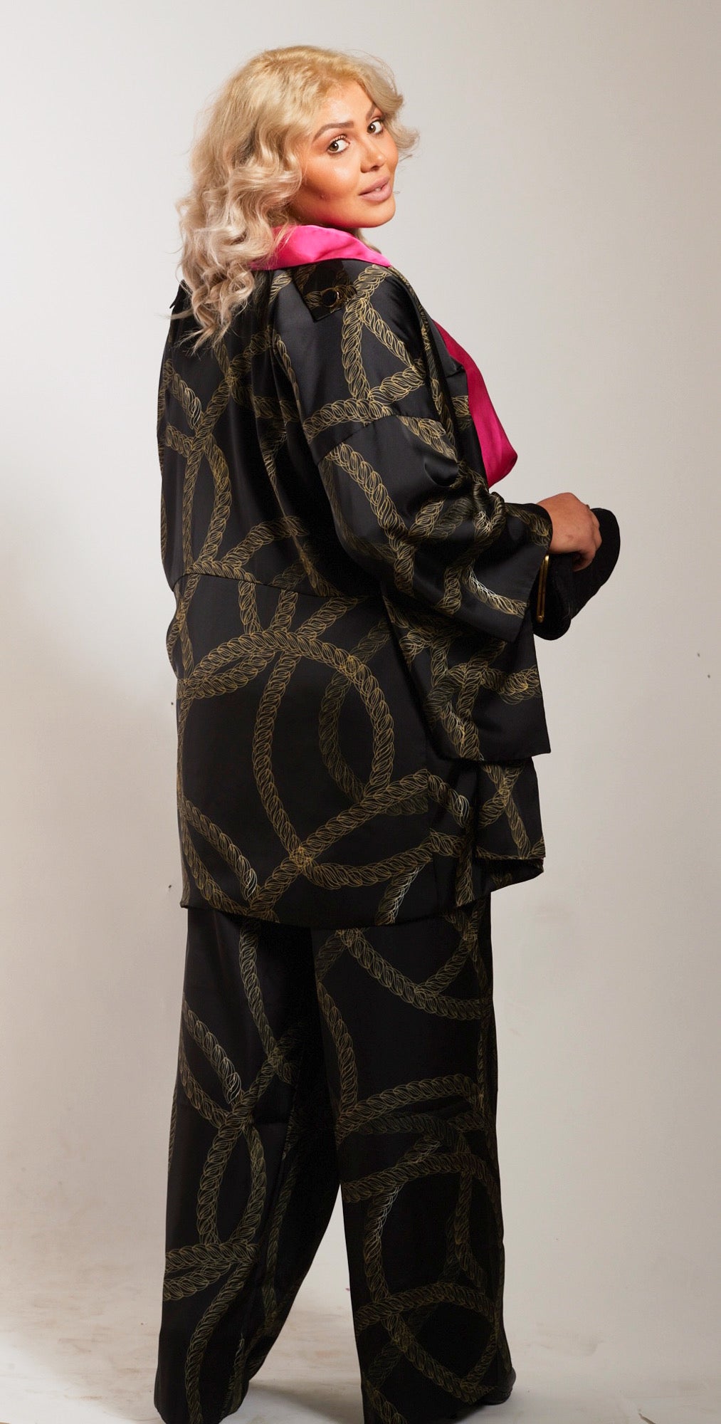 side profile woman modelling black and gold chains printed kimono duster with matching yacht slacks holding a clutch purse