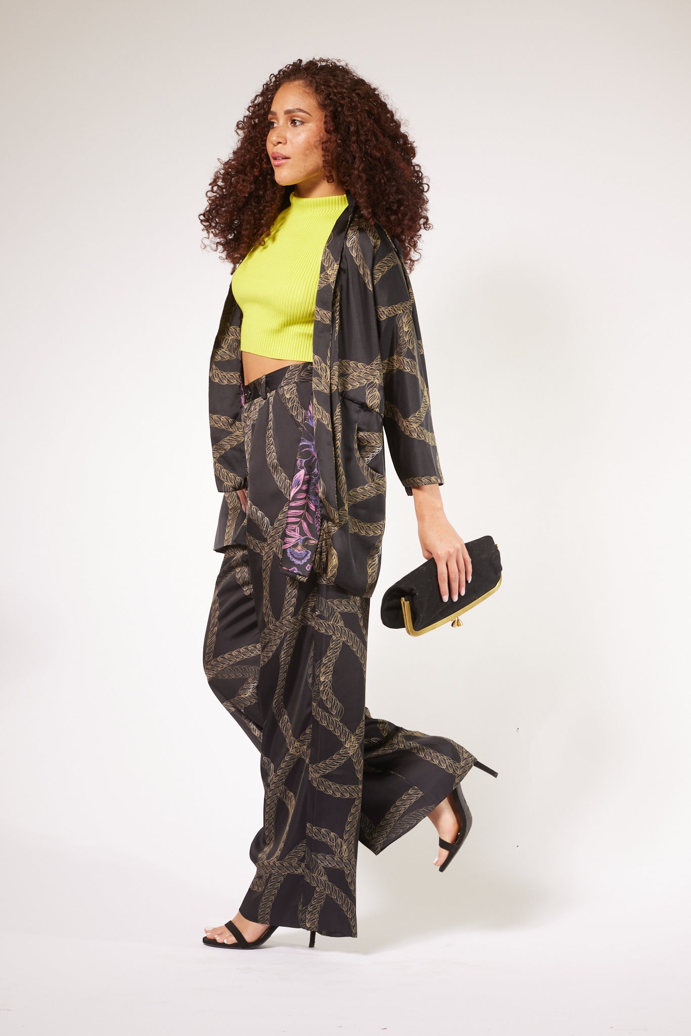 side profile of woman modelling black and gold chains printed kimono duster with matching yacht and high heels 4