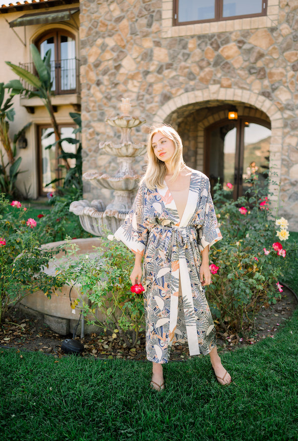 Woman wearing kimono robe in navy toucans standing outside next to flower garden