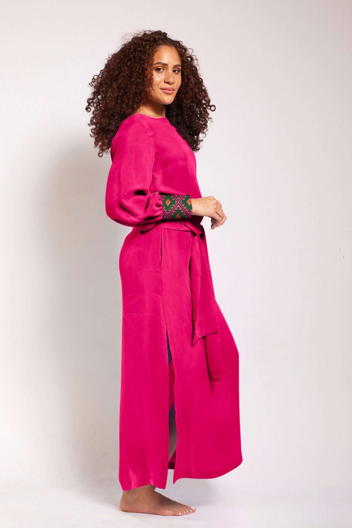 side profile view of woman wearing a magenta kaftan duster with embroidered sleeves made from recycled materials