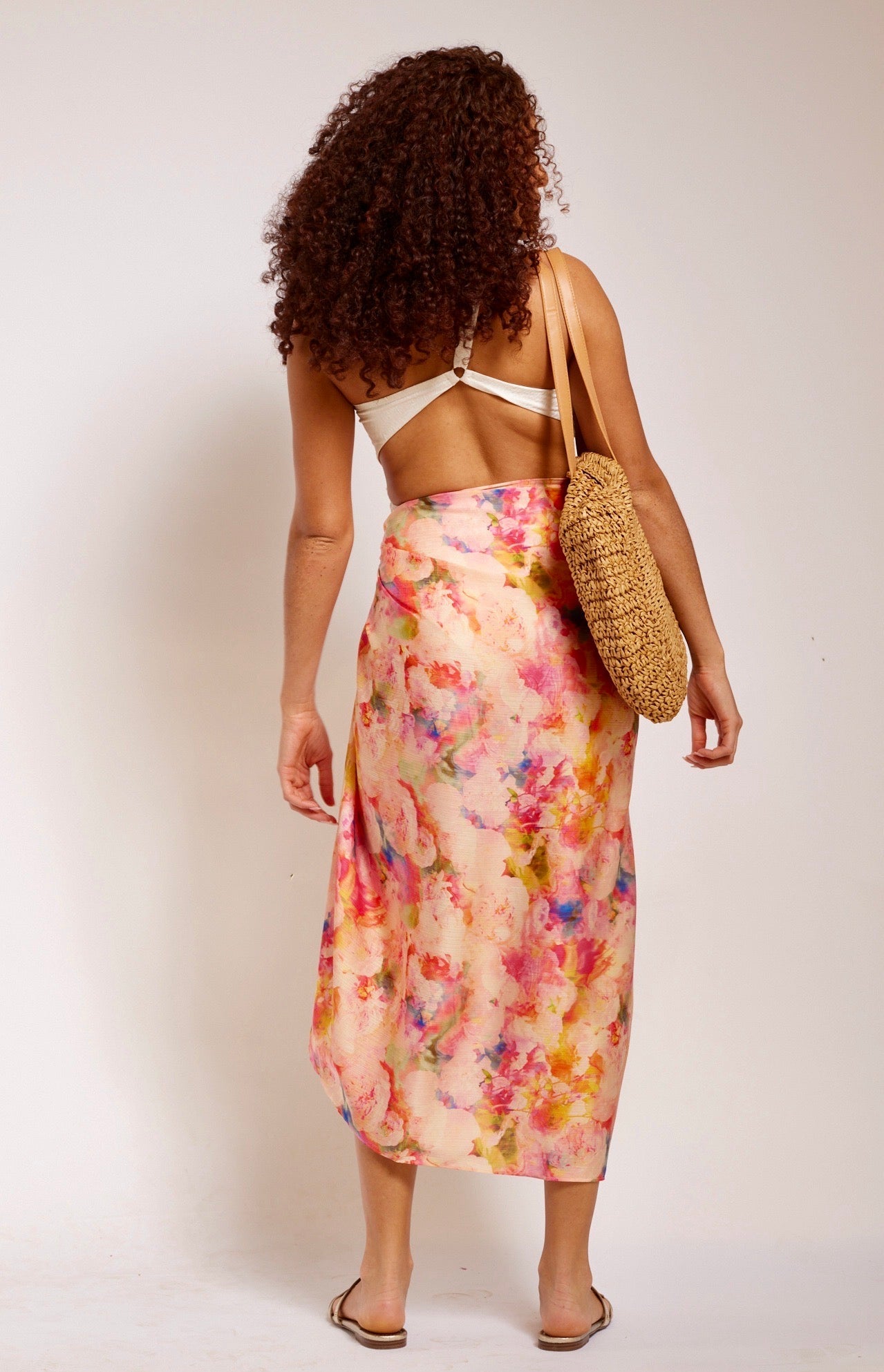back profile of woman standing wearing all over peach floral sarong beachwear made from recycled materials