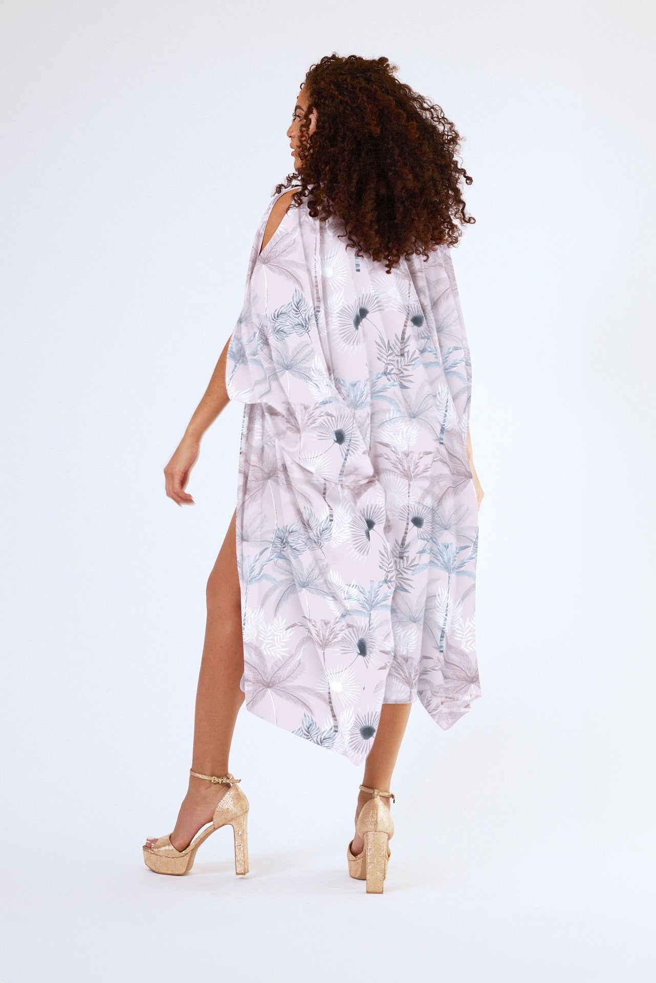 back view of woman wearing all over blush tropical print kaftan duster with front zipper made from recycled materials