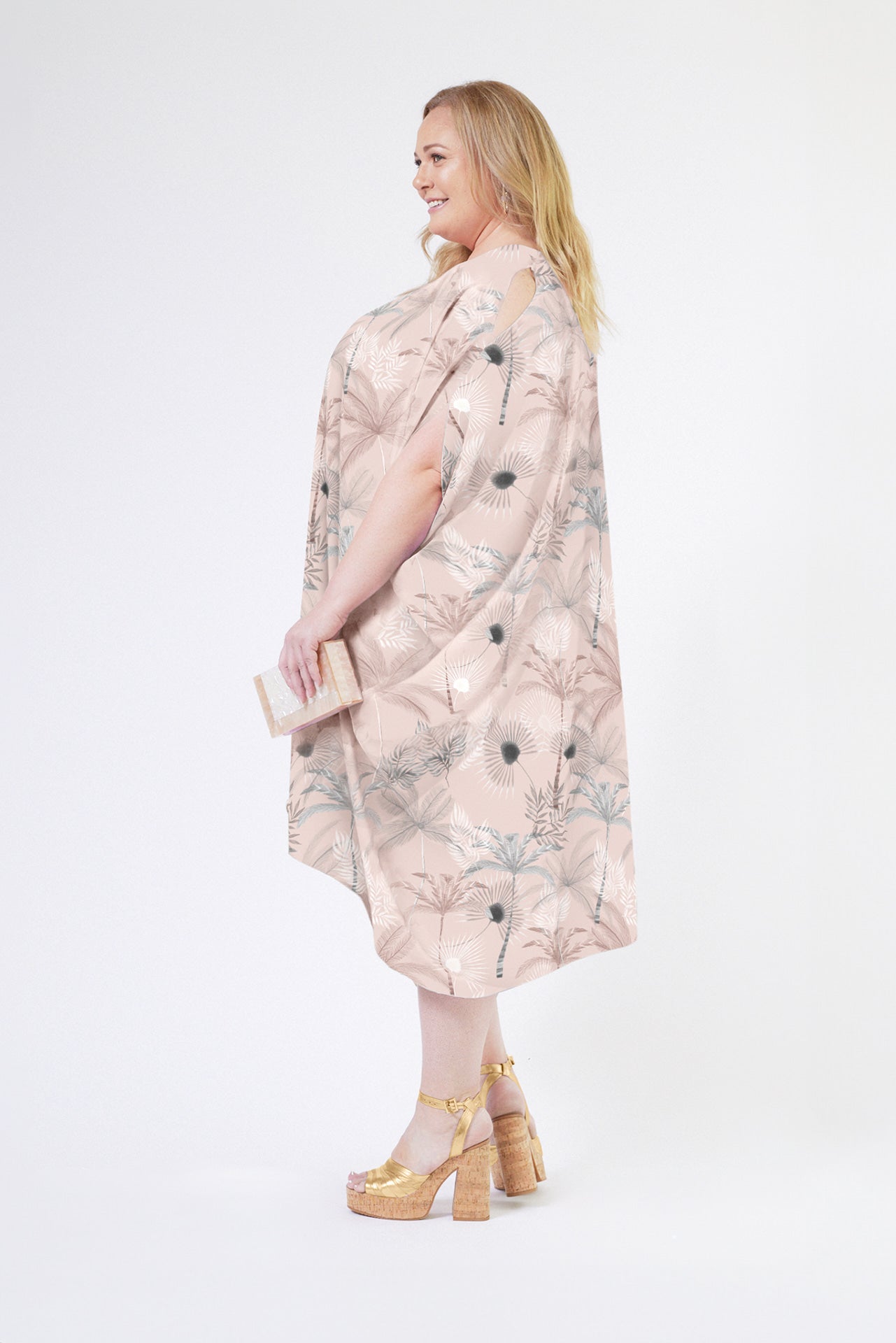 side view of woman wearing all over blush tropical print kaftan duster with front zipper made from recycled materials 2