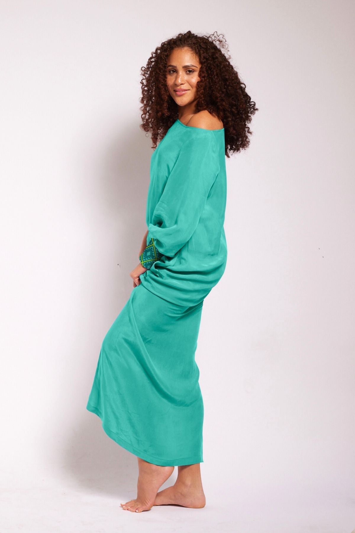 side view of woman wearing turquoise kaftan duster with embroidered sleeves made from recycled materials