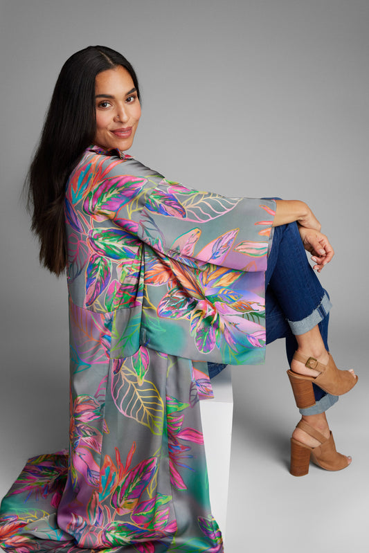 Woman lounging on a chair wearing an all over tropical print kimono duster made from recycled materials 2