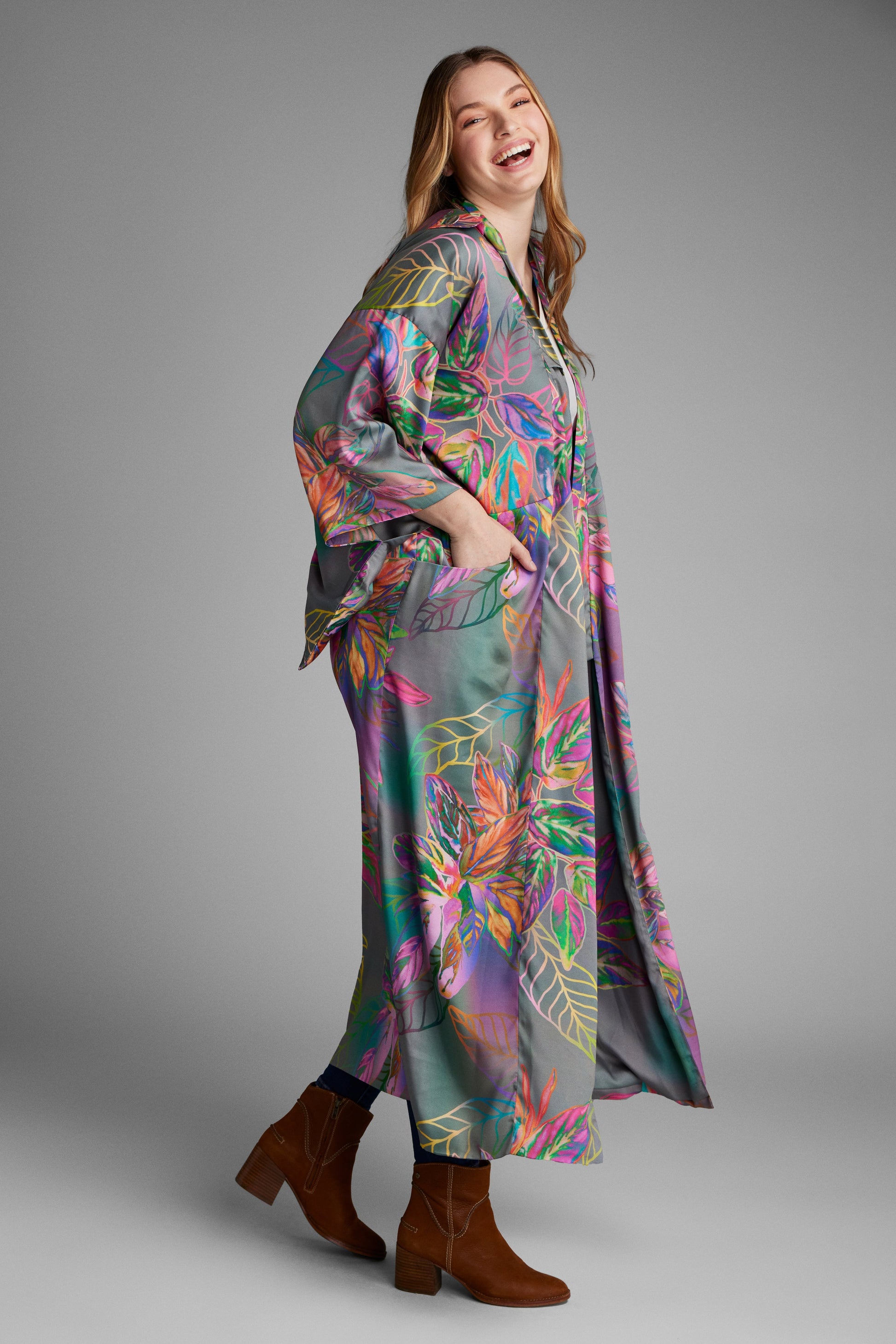Woman standing with hand in pocket wearing an all over tropical print kimono duster made from recycled materials 2