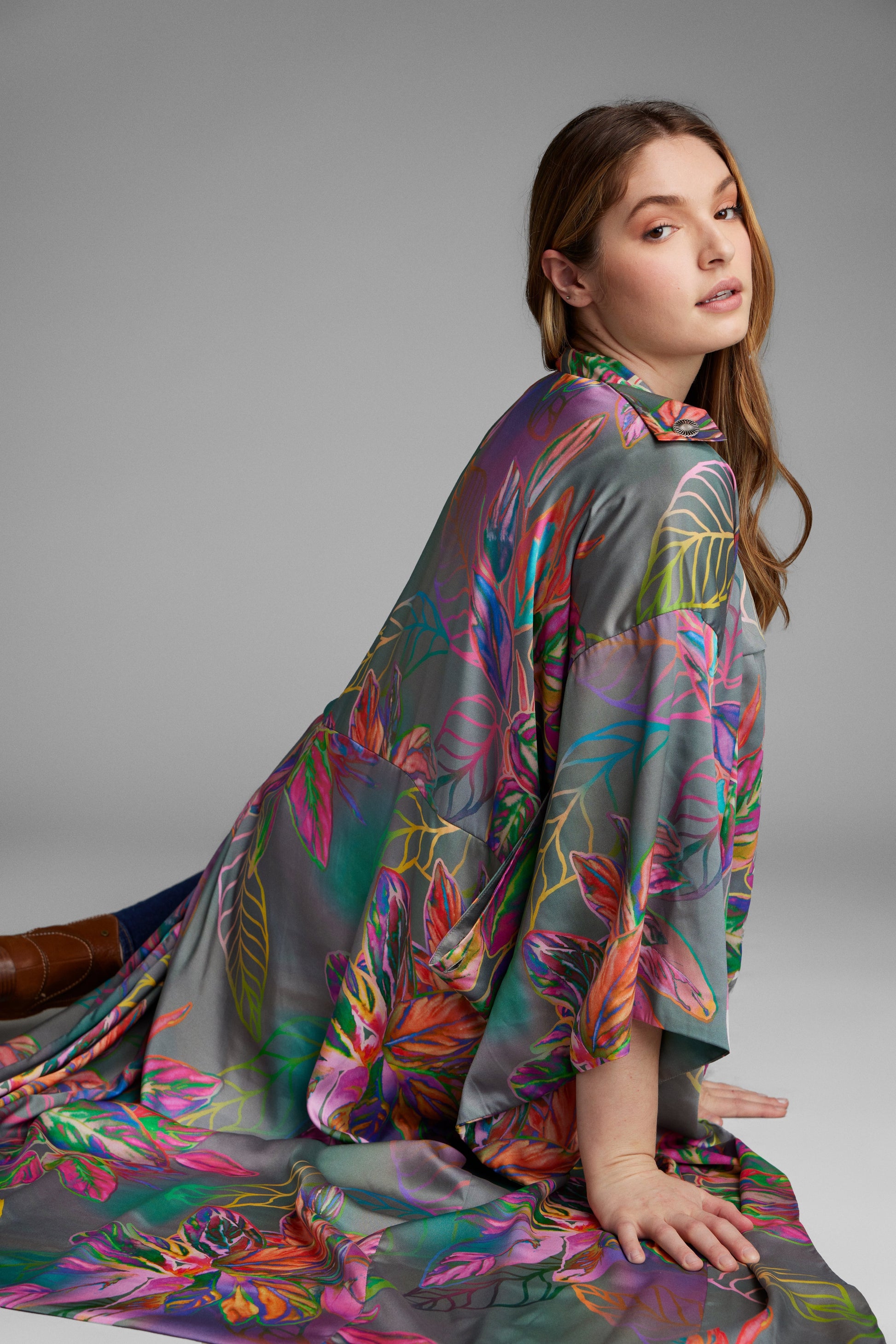 Woman sitting on the floor wearing an all over tropical print kimono duster made from recycled materials