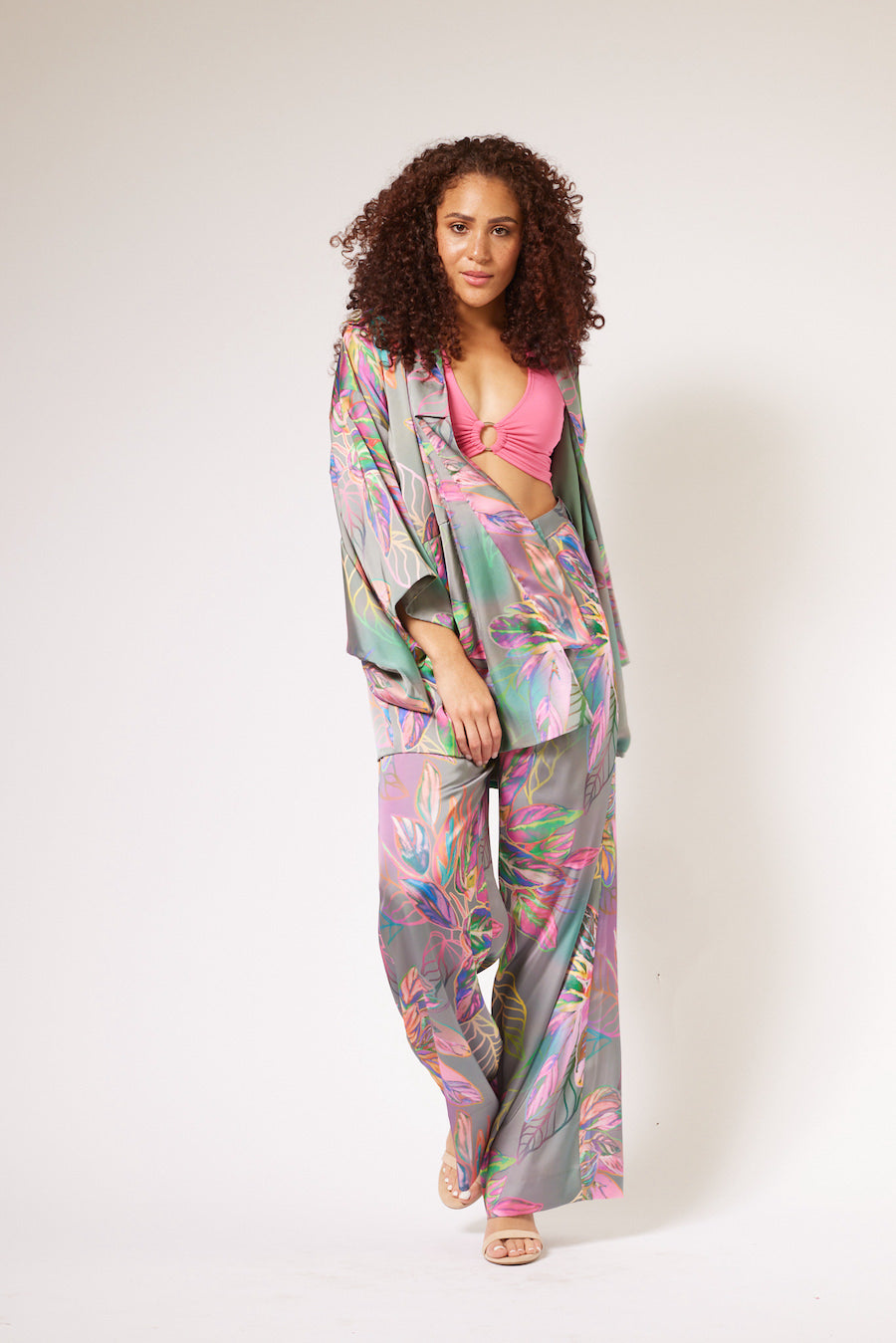 Woman standing and wearing an all over tropical print kimono duster and yacht pants made from recycled materials