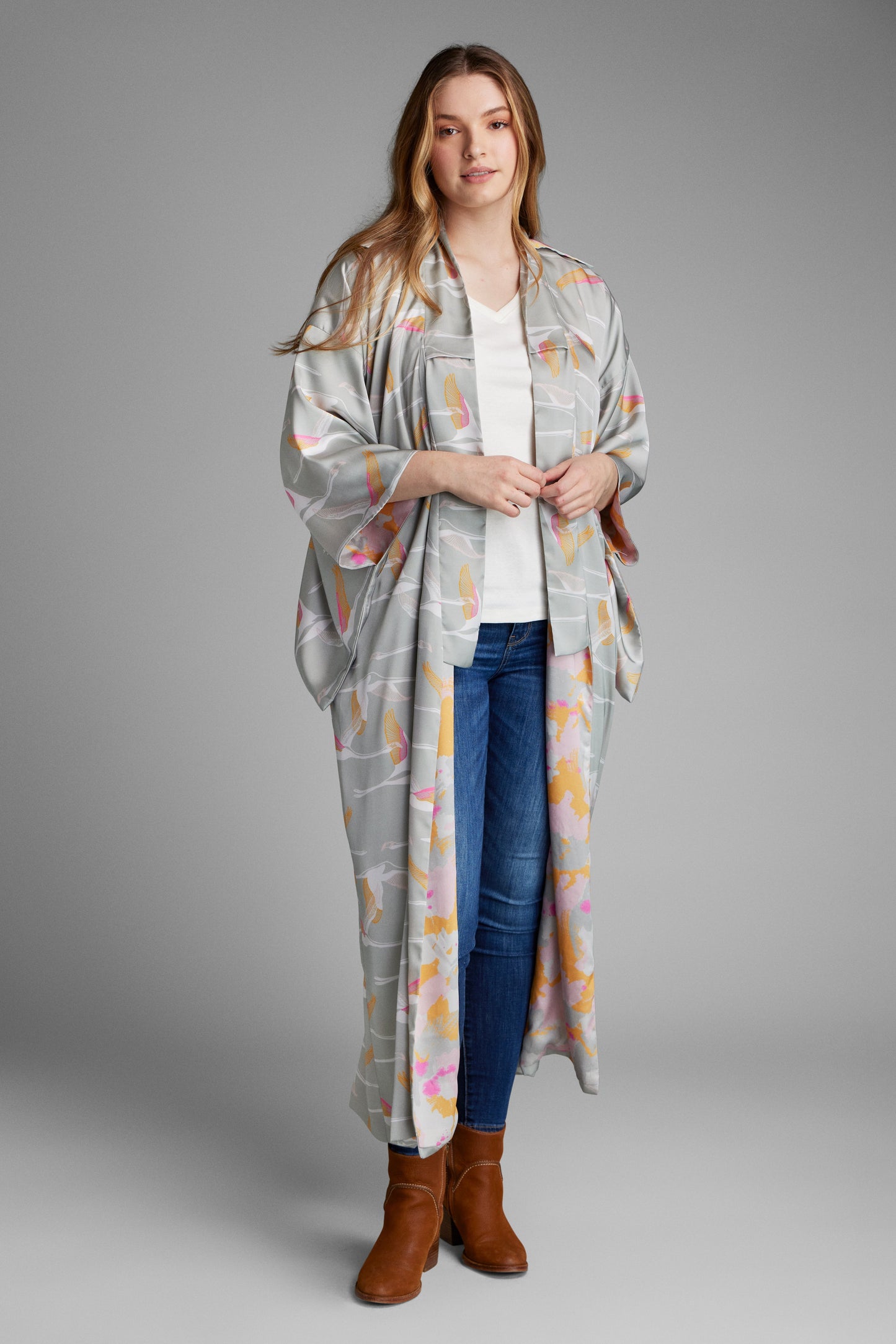 Woman standing wearing a grey pink and gold colored crane print kimono duster made from recycled materials