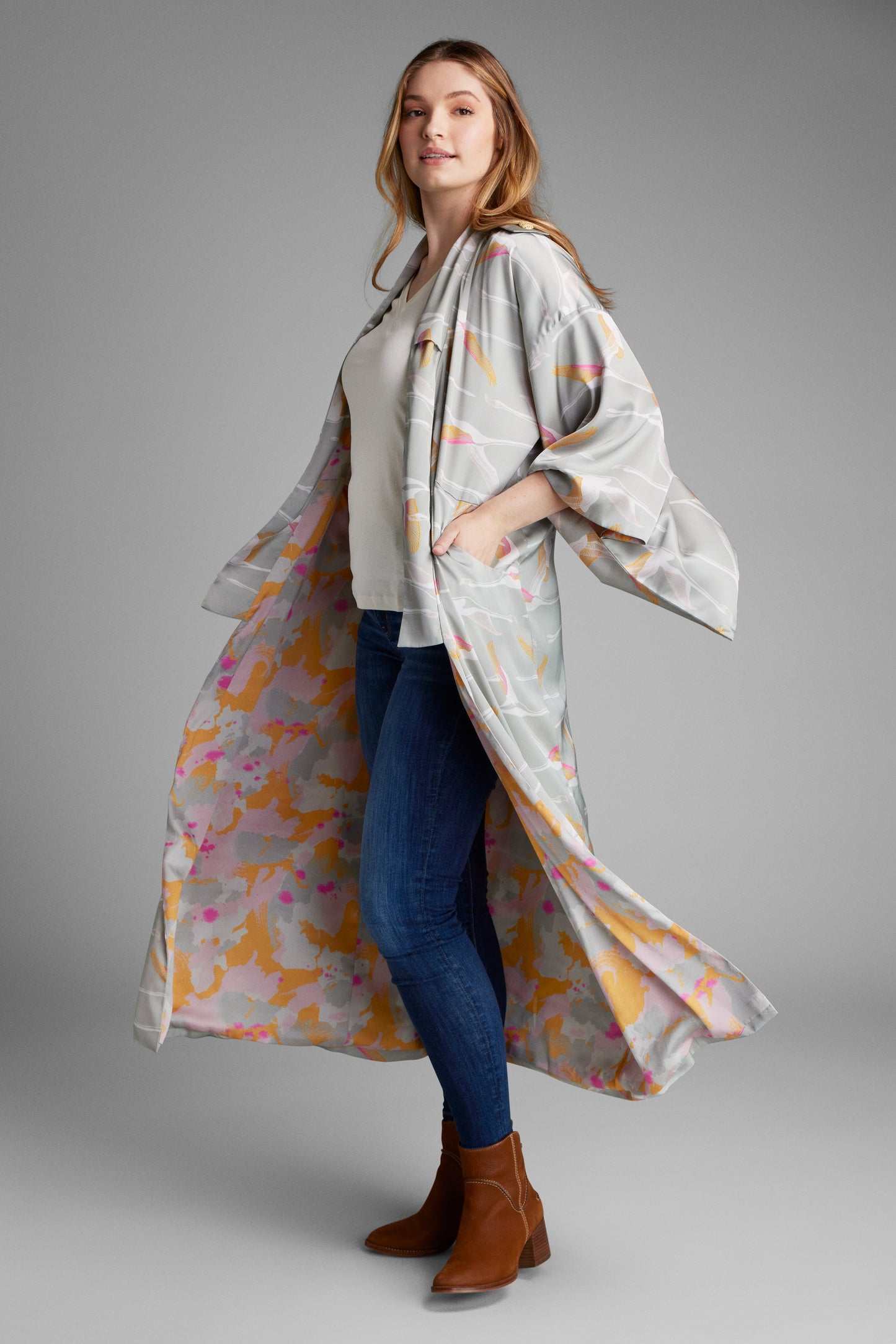 Woman twirling wearing a grey pink and gold colored crane print kimono duster made from recycled materials