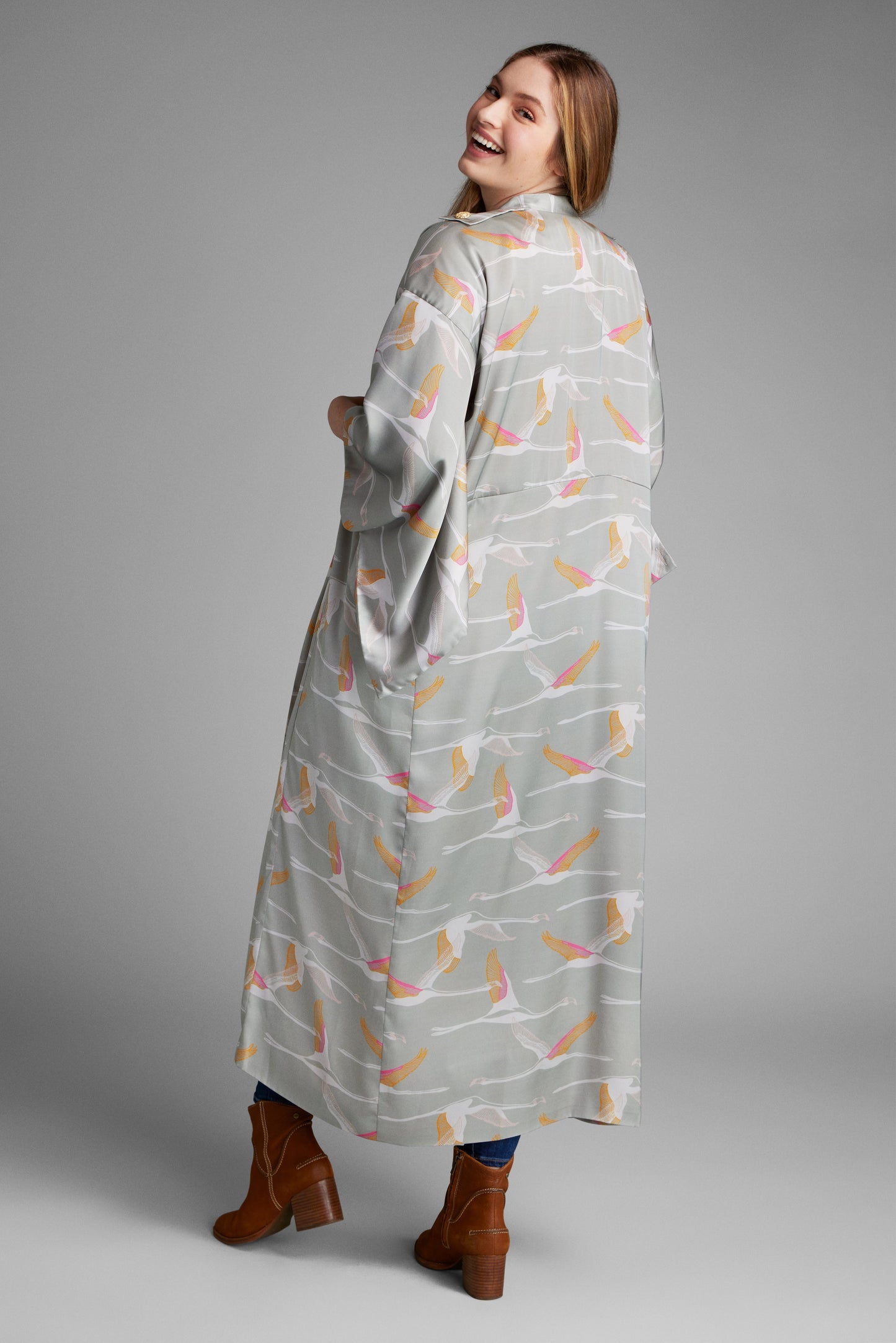 Back profile view of woman wearing a grey pink and gold colored crane print kimono duster made from recycled materials 3