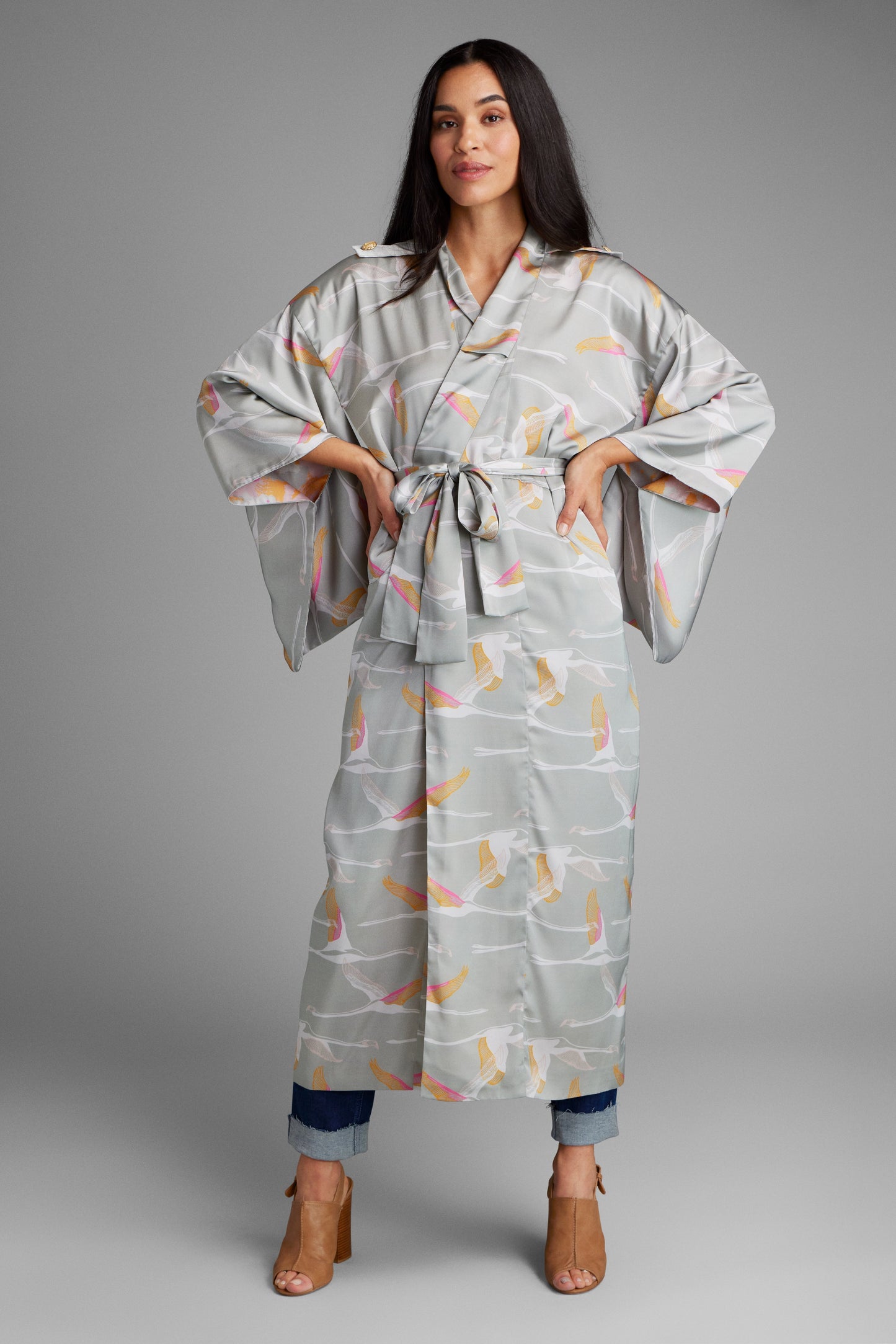Woman standing with hands at her waist wearing a grey pink and gold colored crane print kimono duster made from recycled materials