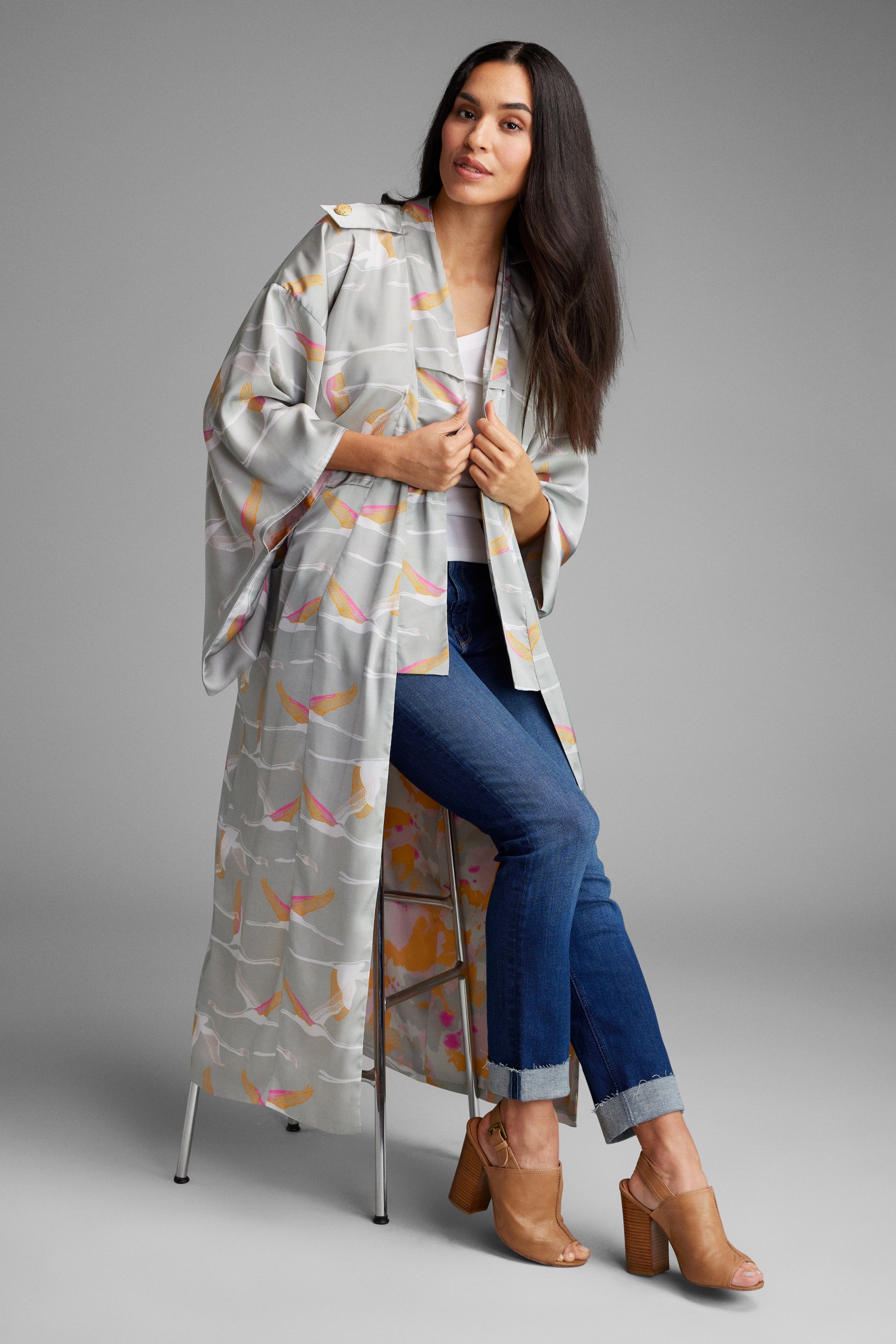 Woman sitting on a stool wearing a grey and pink colored crane patterned kimono duster made from recycled materials