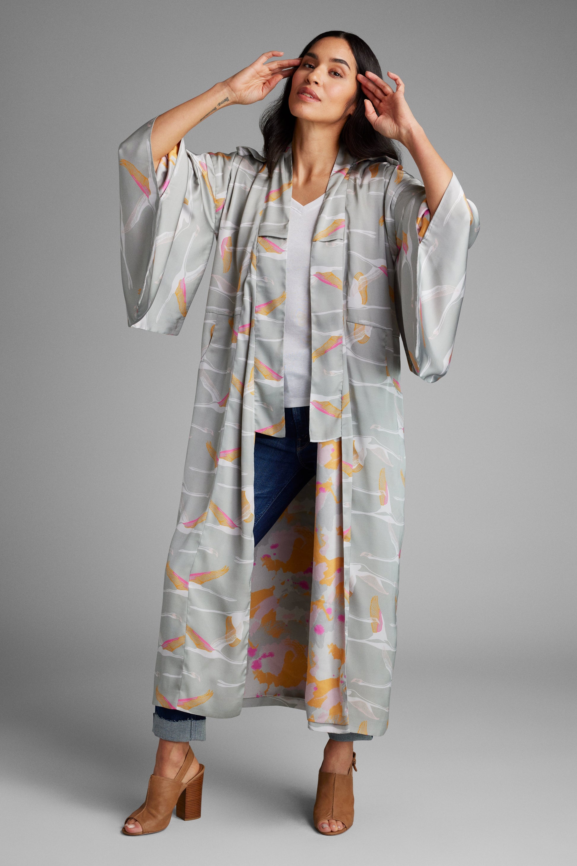 Woman standing with hands on her face wearing a grey and pink colored crane patterned kimono duster made from recycled materials