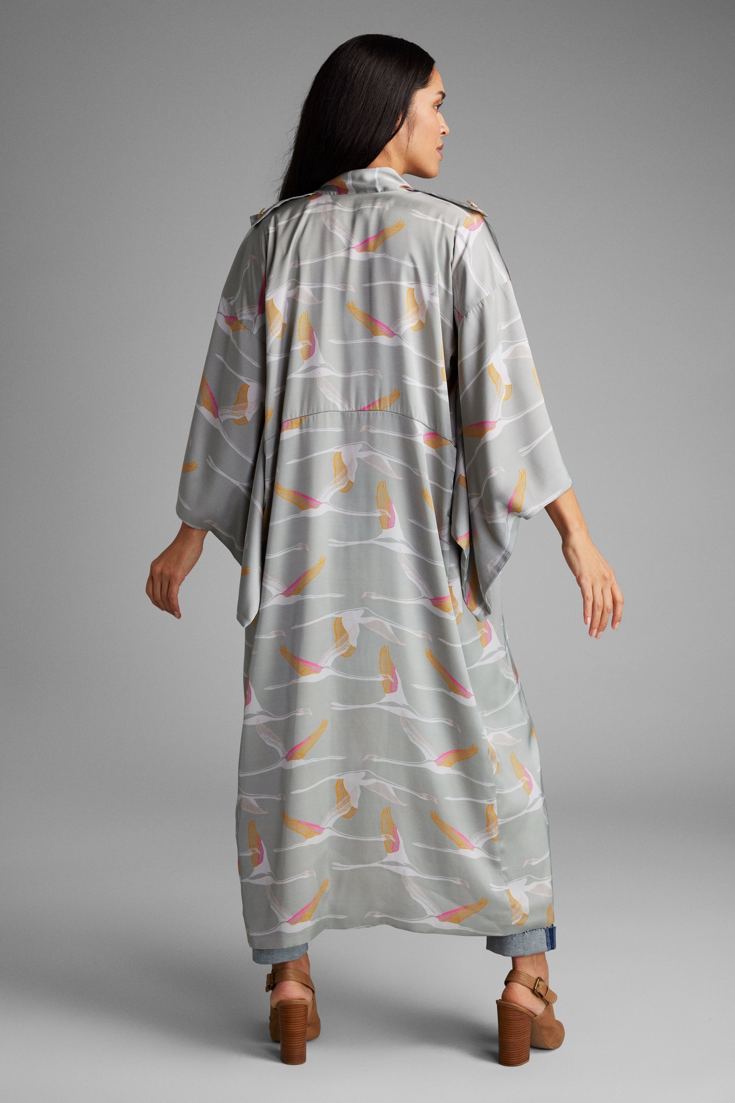 back view of woman standing with hands on her face wearing a grey and pink colored crane patterned kimono duster made from recycled materials