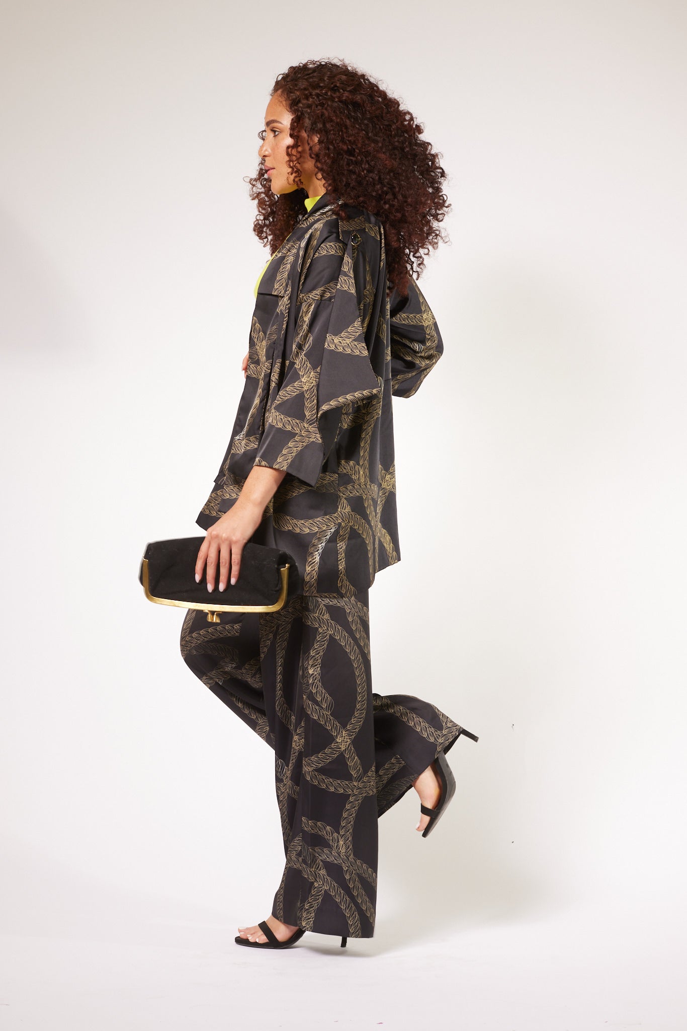 side profile of woman wearing black and gold chain printed yacht slacks and matching kimono duster made from recycled textiles 2