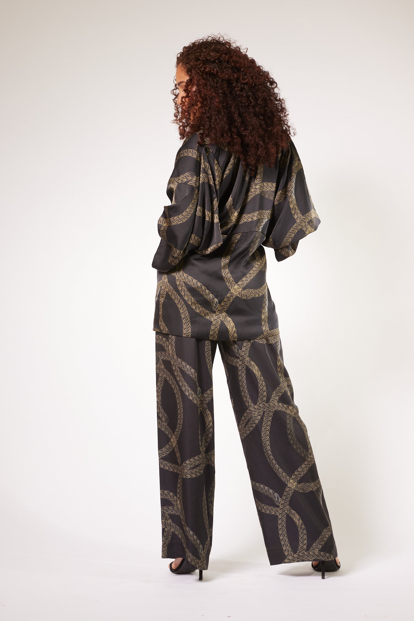 back profile of woman wearing black and gold chain printed yacht slacks and matching kimono duster made from recycled textiles