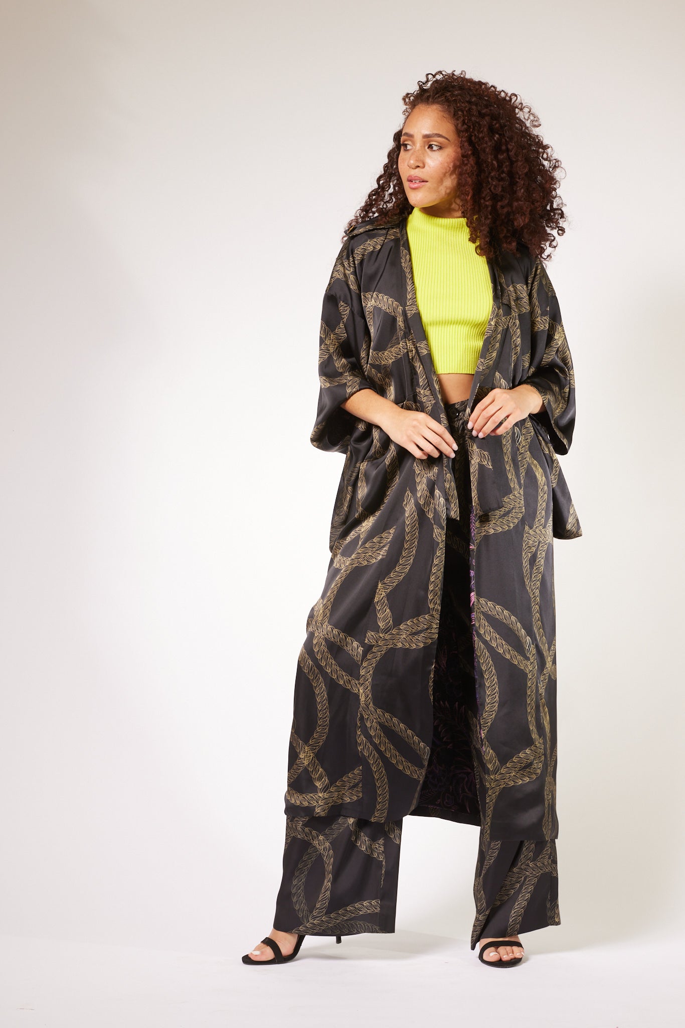 side profile of woman wearing black and gold chain printed yacht slacks and matching kimono duster made from recycled materials