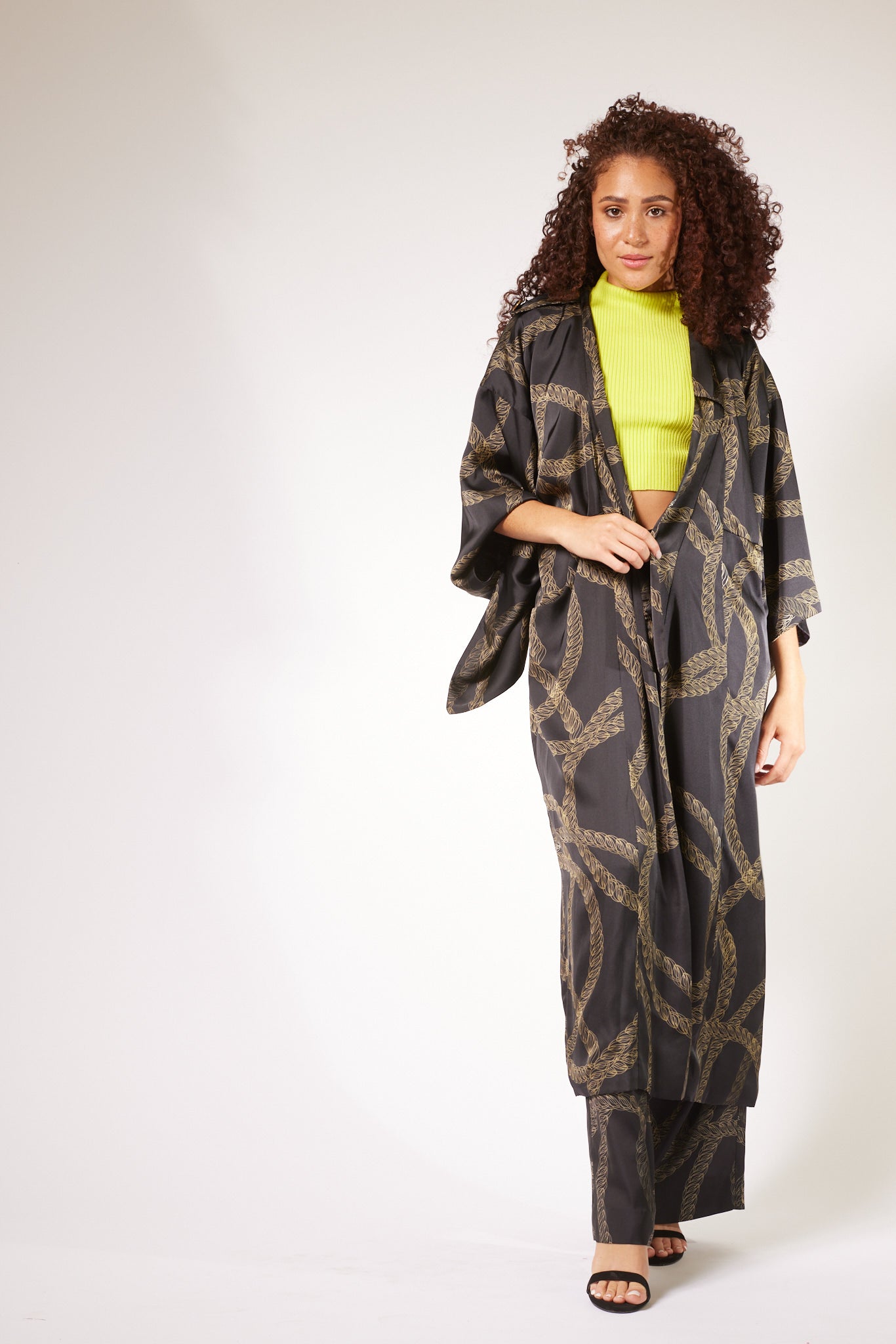 side profile of woman wearing black and gold chain printed yacht slacks and matching kimono duster made from recycled materials 2
