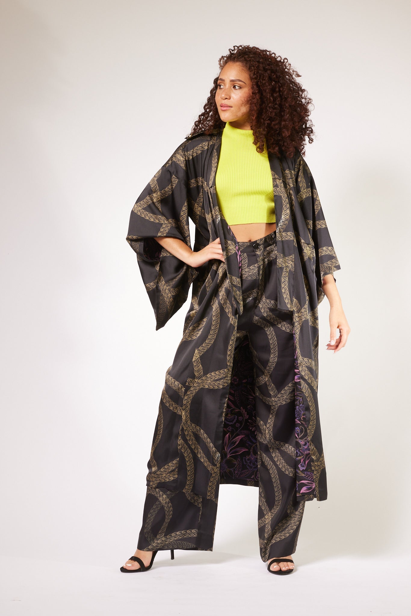 front profile of woman hands on hips wearing black and gold chain printed yacht slacks made from recycled textiles 2