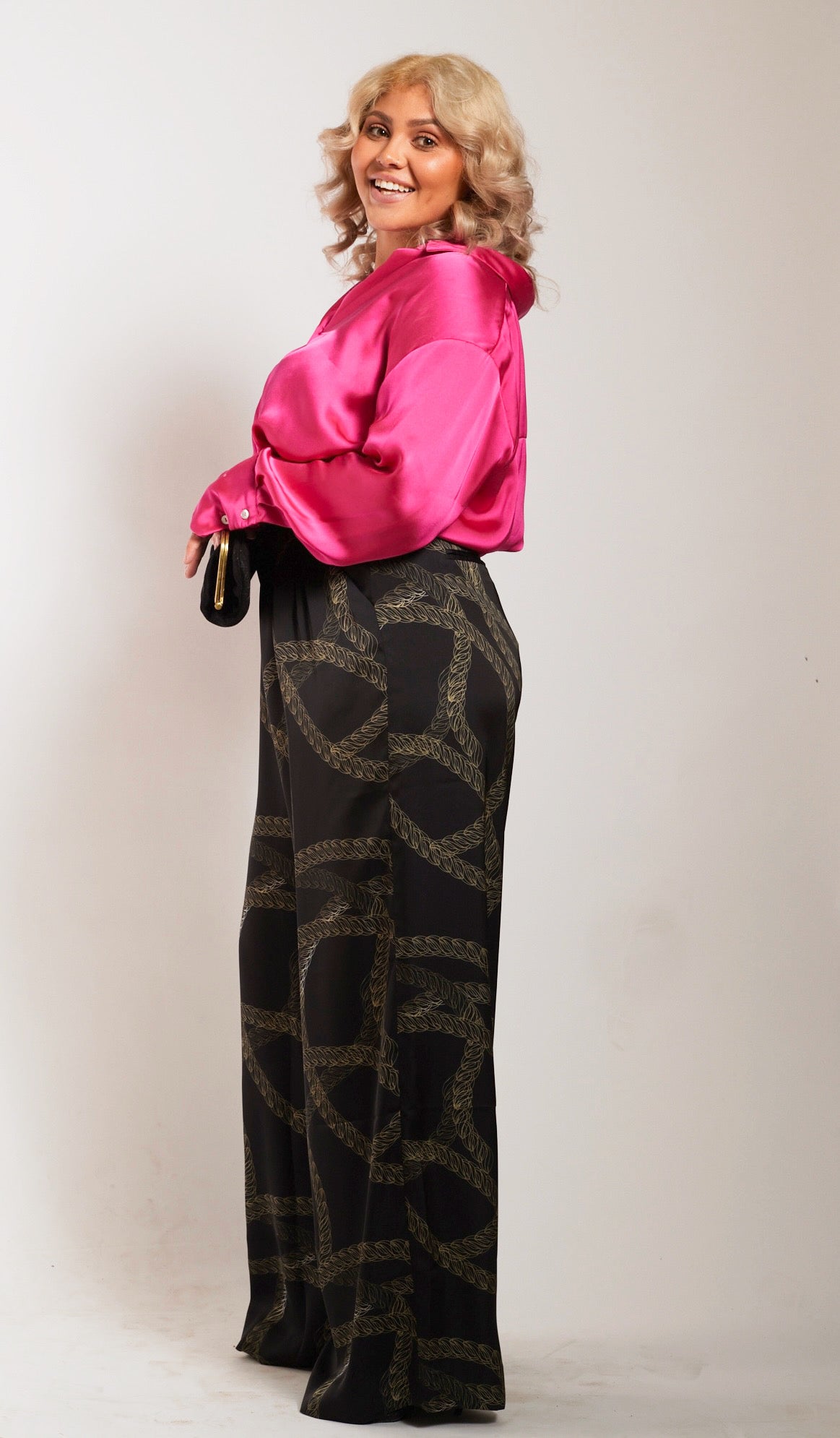 side profile of woman wearing black and gold chain printed yacht slacks and pink blouse 2
