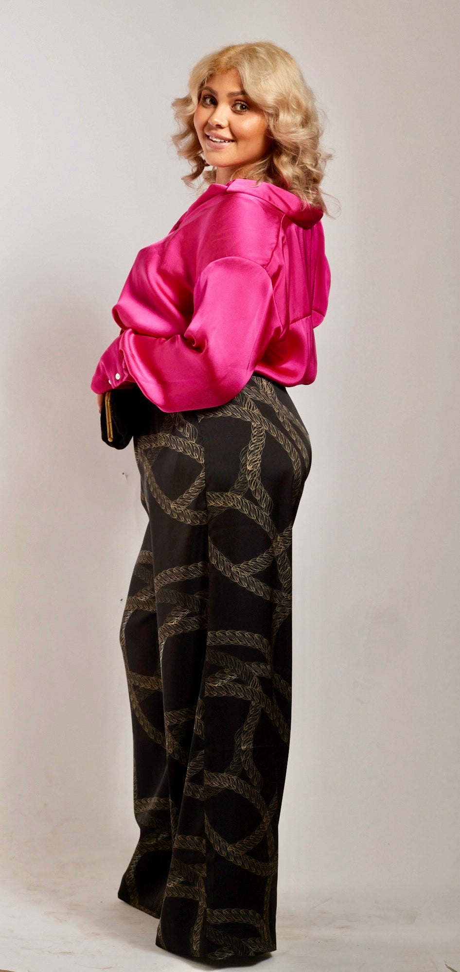 side profile of woman wearing black and gold chain printed yacht slacks and pink blouse 3