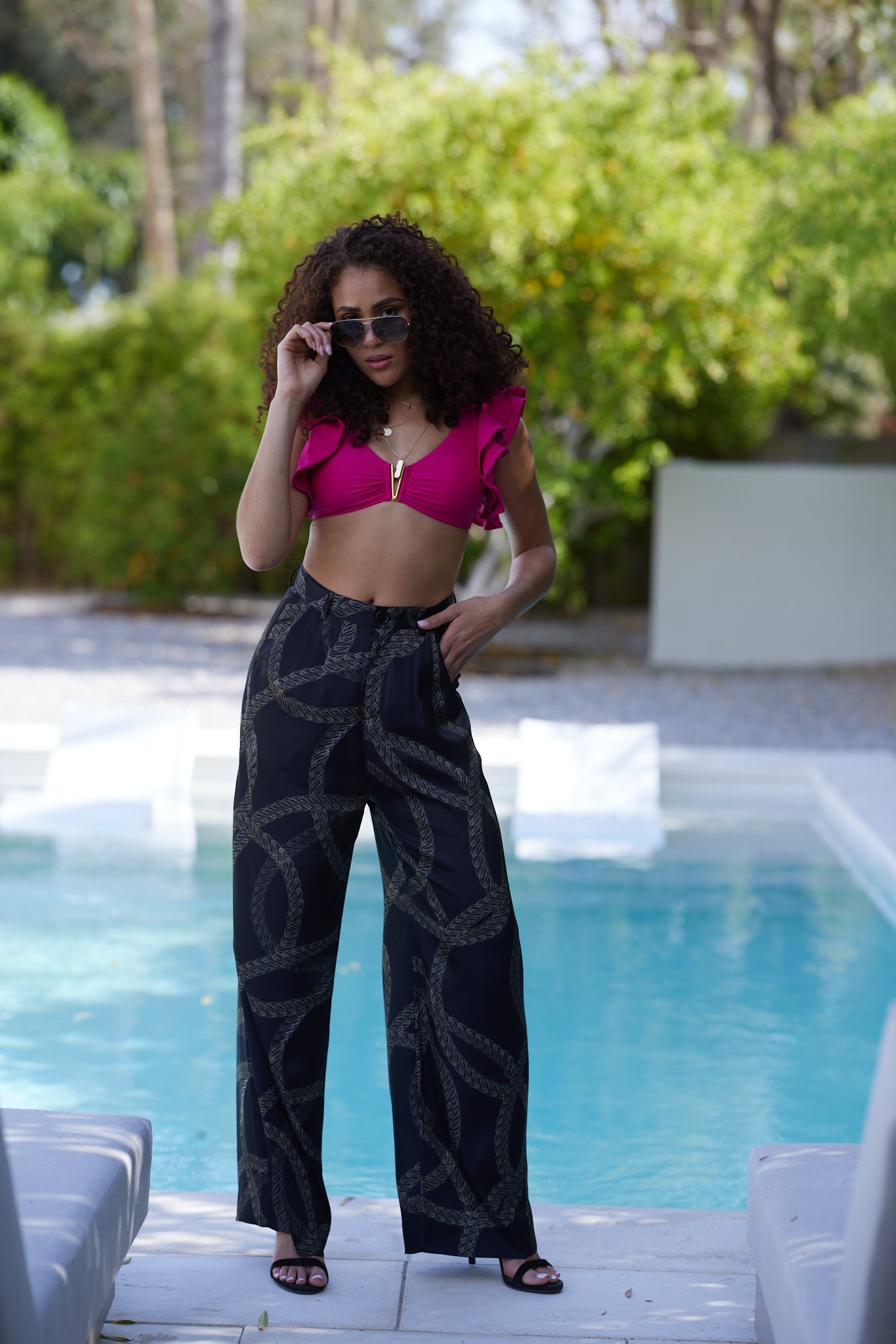 woman poolside wearing gold and black chain printed yacht slacks styling sunglasses and heels
