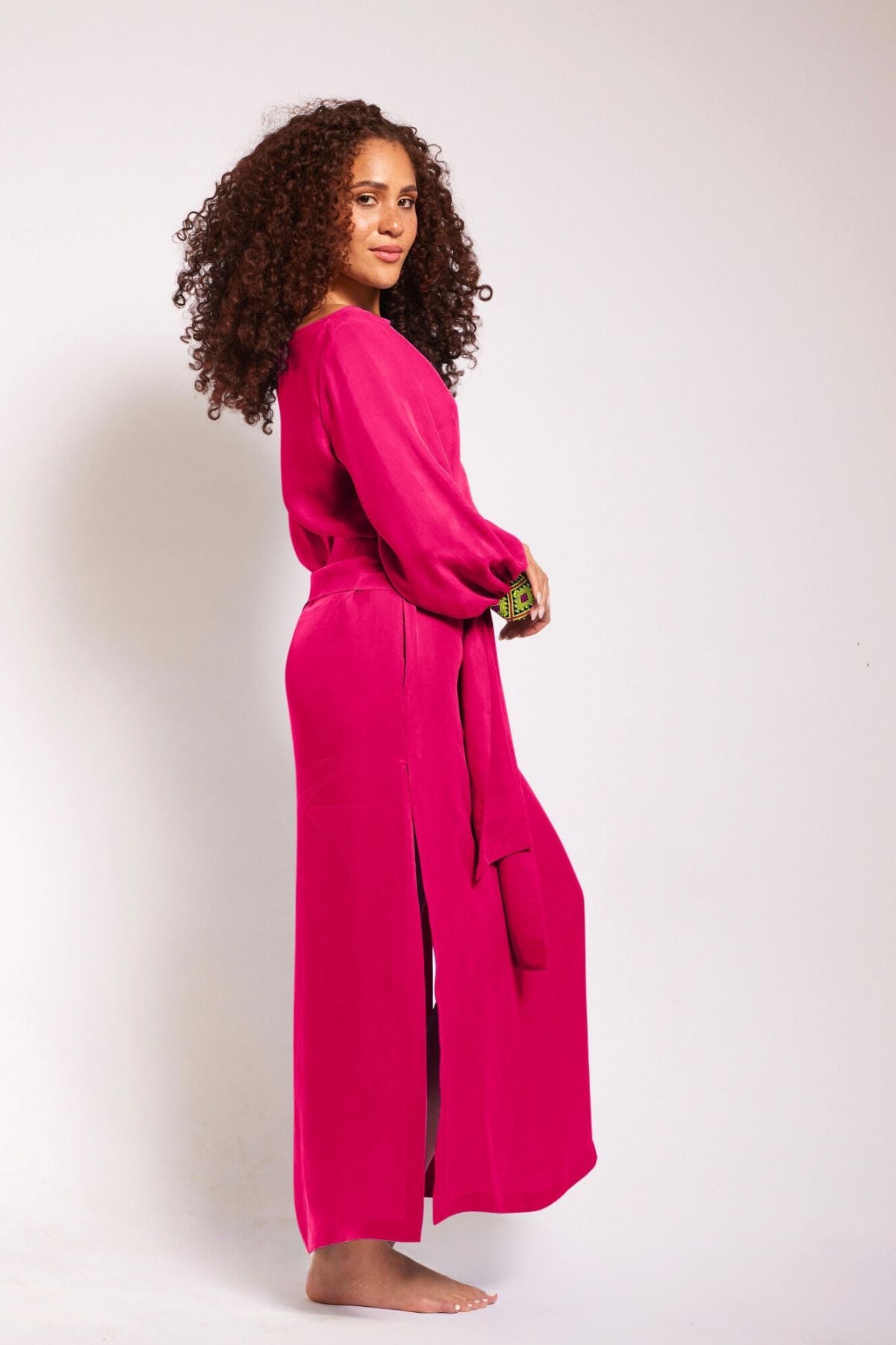 side view of woman wearing a magenta kaftan duster with embroidered sleeves made from recycled materials