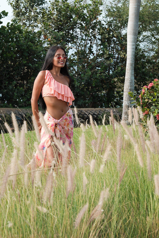woman outside modelling all over peach floral sarong beachwear made from recycled materials