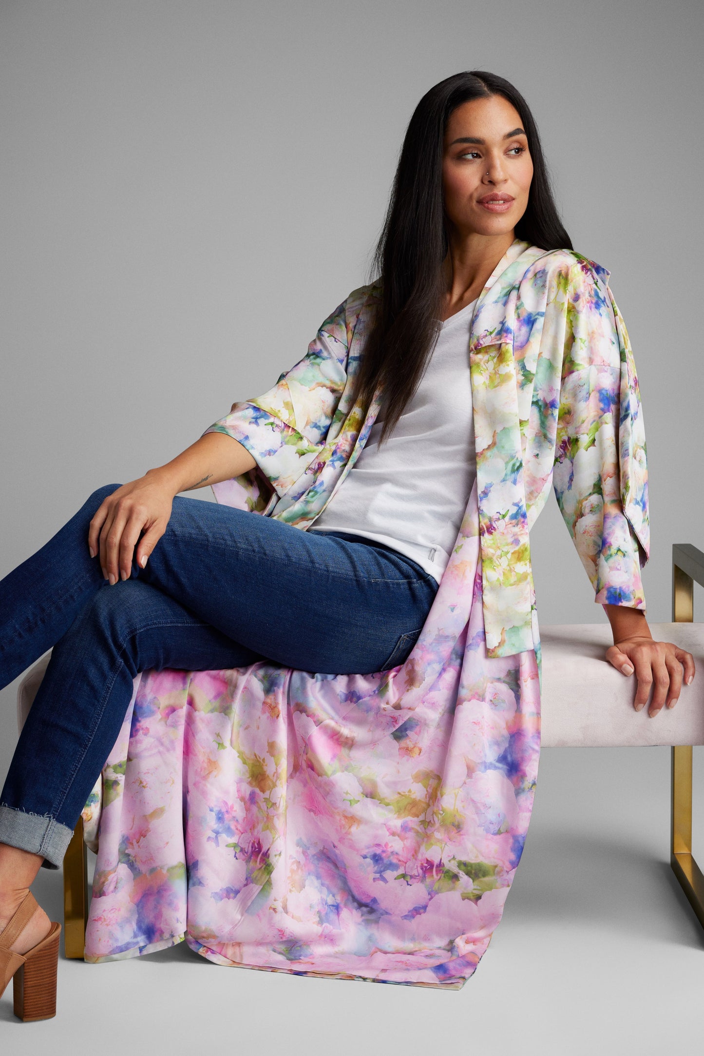 Woman lounging on a chair wearing an all over floral print kimono duster made from recycled materials