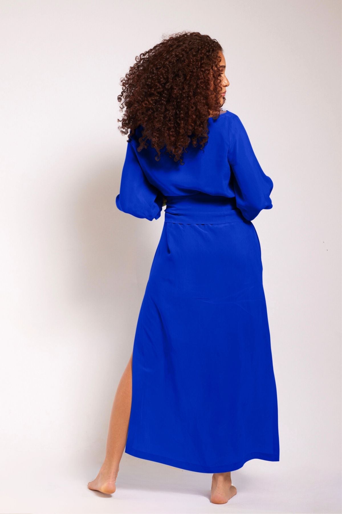 back view of woman wearing a royal blue kaftan duster with embroidered sleeves made from recycled materials