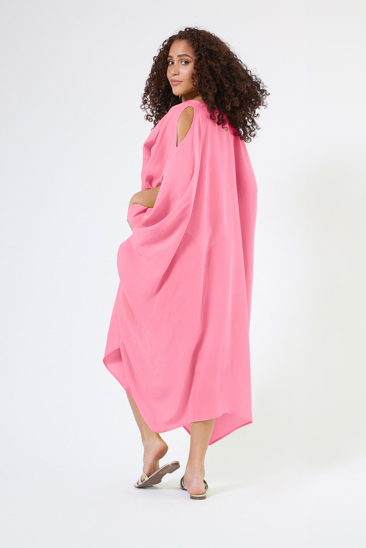 back view of woman wearing bubble gum pink kaftan duster with front zipper made from recycled materials
