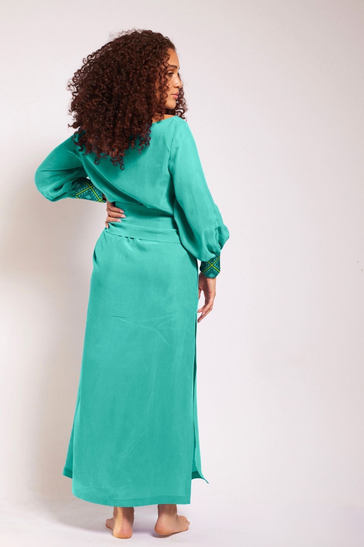 back view of woman wearing turquoise kaftan duster with embroidered sleeves made from recycled materials