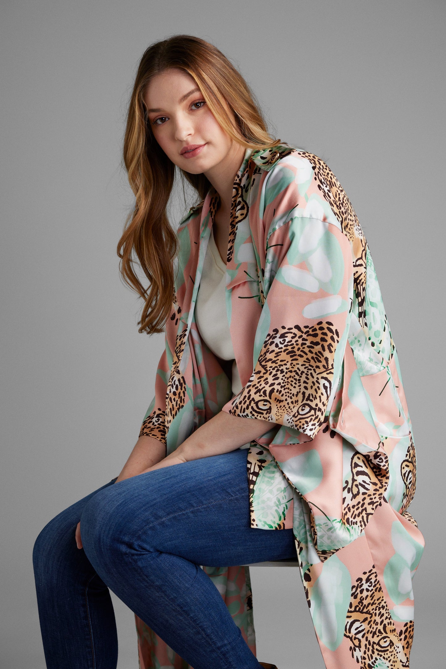 Woman on a stool wearing an all over tropical animal print duster with pockets made from recycled materials